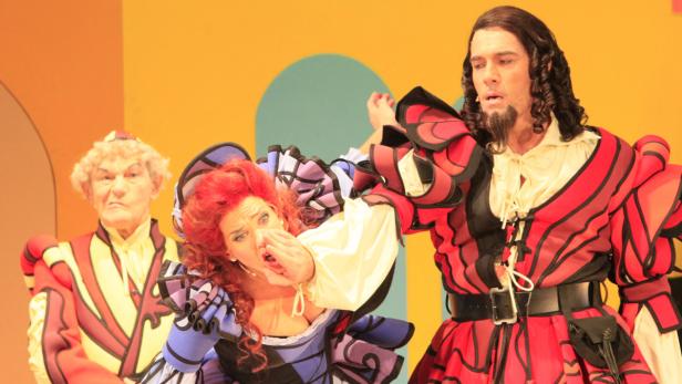 Szene aus einer Theateraufführung mit drei Darstellern in farbenfrohen Kostümen.