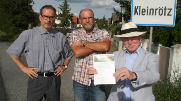 Drei Männer stehen vor einem Ortsschild von Kleinrötz, einer hält ein Dokument in der Hand.