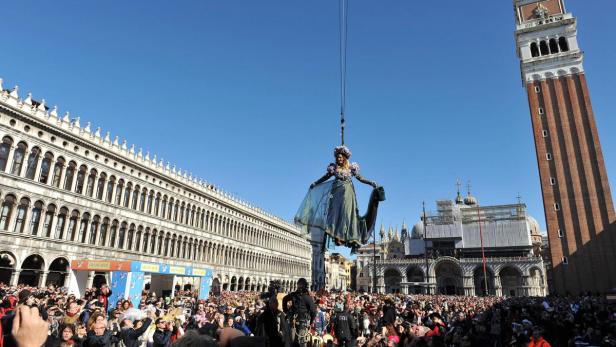 Eine Frau in einem Kostüm schwebt an einem Kran über dem Markusplatz in Venedig.