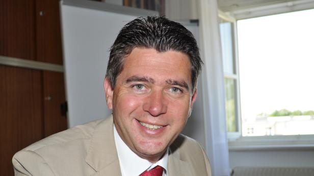 Ein lächelnder Mann in einem hellen Anzug und roter Krawatte.