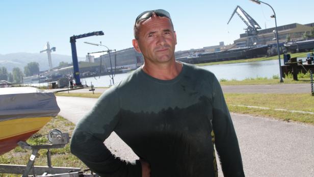 Ein Mann posiert vor einer Werft mit einem kleinen Boot im Vordergrund.