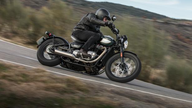 Ein Motorradfahrer fährt auf einer Triumph Bobber eine kurvenreiche Straße entlang.