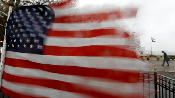 Eine amerikanische Flagge weht im Wind, während eine Person im Hintergrund vorbeigeht.