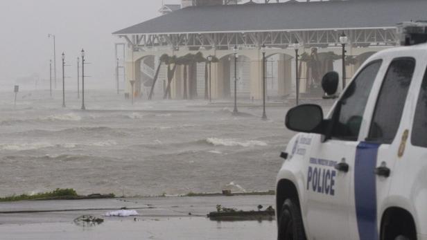 Ein Küstenort steht während eines Sturms unter Wasser, im Vordergrund ein Polizeiauto.