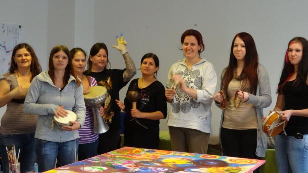 Eine Gruppe von Frauen musiziert mit verschiedenen Instrumenten vor einem bunten Bild.