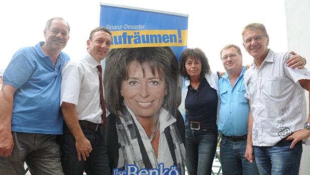 Eine Gruppe von Menschen posiert vor einem Wahlplakat von Ilse Benkö.