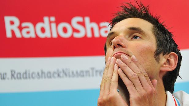 Ein Mann hält seine Hände vor das Gesicht, im Hintergrund ein RadioShack-Logo.