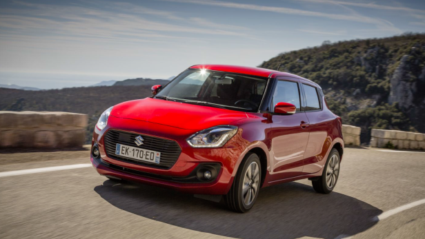 Ein roter Suzuki Swift fährt auf einer kurvenreichen Straße.