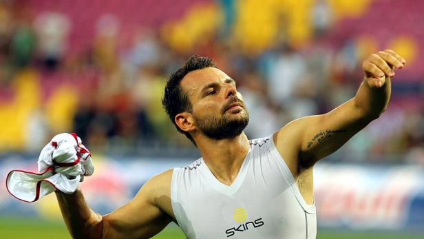 Ein Mann in Sportkleidung hält ein Trikot in der Hand und blickt nach oben.