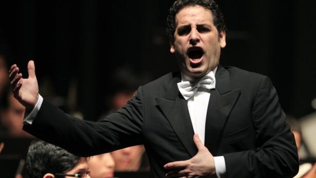 Ein Opernsänger singt in einem schwarzen Anzug mit Fliege auf der Bühne.