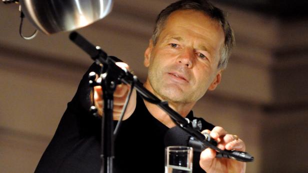 Ein Mann spricht in ein Mikrofon vor einem unscharfen Hintergrund.