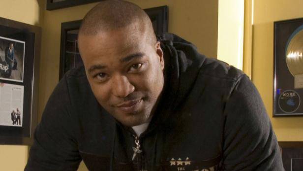 Ein Mann mit rasiertem Kopf und dunklem Kapuzenpullover blickt in die Kamera.