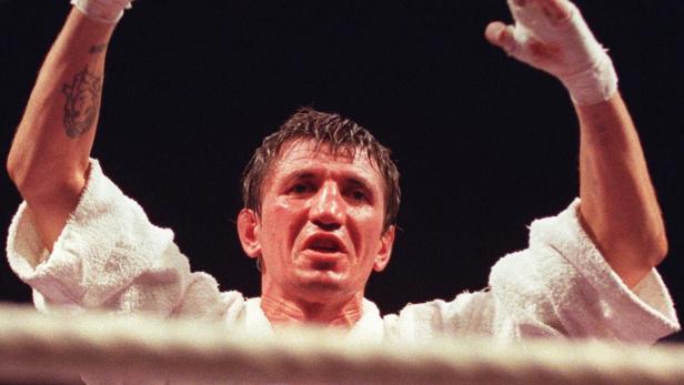 Ein Boxer mit erhobenen, bandagierten Händen im Ring.