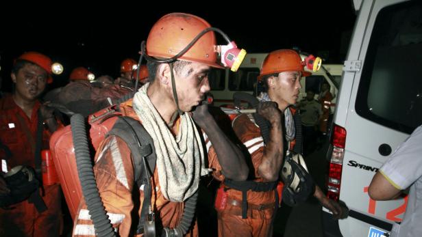 Erschöpfte Bergleute nach einem Einsatz in ihren Arbeitsanzügen und Helmen vor einem Rettungswagen.