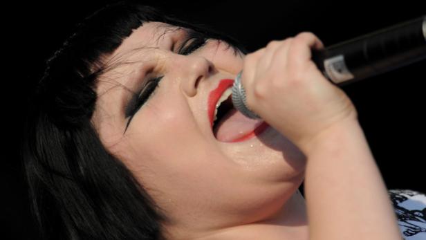 Eine Sängerin mit rotem Lippenstift singt in ein Mikrofon.