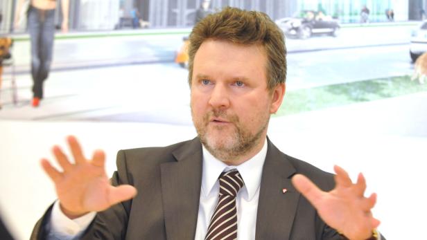 Ein Mann im Anzug gestikuliert vor einem unscharfen Hintergrund.