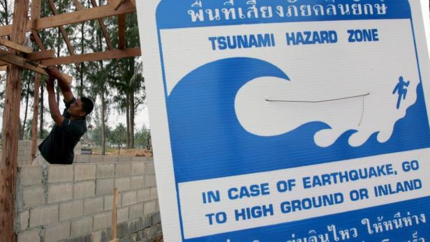 Ein Mann arbeitet an einem Gebäude neben einem Schild, das vor einer Tsunami-Gefahrenzone warnt.