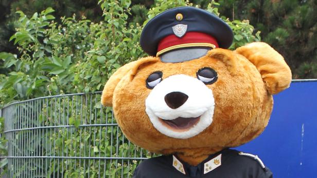 Ein Teddybär-Maskottchen in Polizeiuniform mit Mütze lächelt.