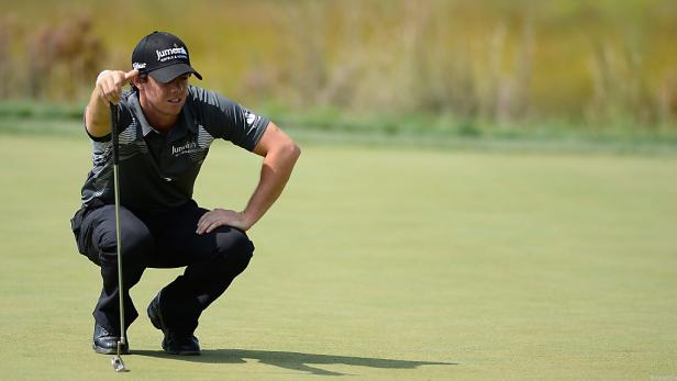 Ein Golfspieler kauert auf dem Grün und zielt mit seinem Putter.