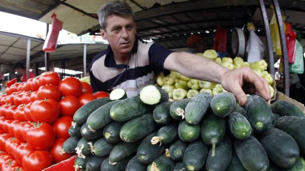 Ein Mann steht an einem Marktstand mit Tomaten, Gurken und Paprika.