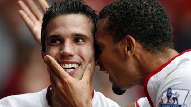 Ein Fußballspieler berührt das Gesicht eines lächelnden Mitspielers, während dieser ihm etwas ins Ohr flüstert.