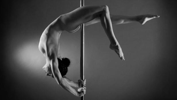 Eine Frau vollführt eine akrobatische Übung an einer Stange.