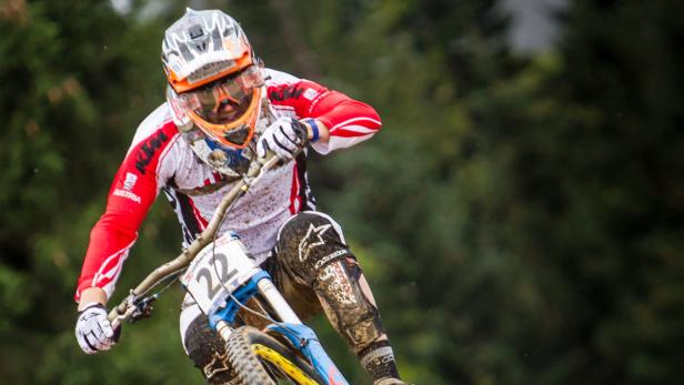 Ein Mountainbike-Fahrer in voller Montur rast einen schlammigen Hang hinunter.