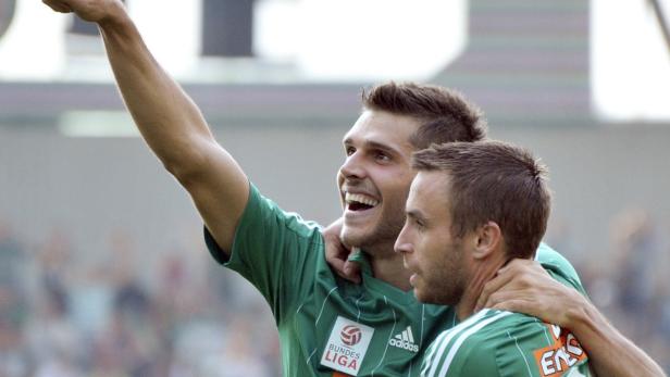 Zwei Fußballspieler in grünen Trikots feiern einen Sieg.