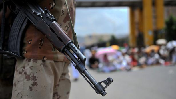 Ein Soldat mit einem Gewehr im Vordergrund, im Hintergrund eine Menschenmenge.