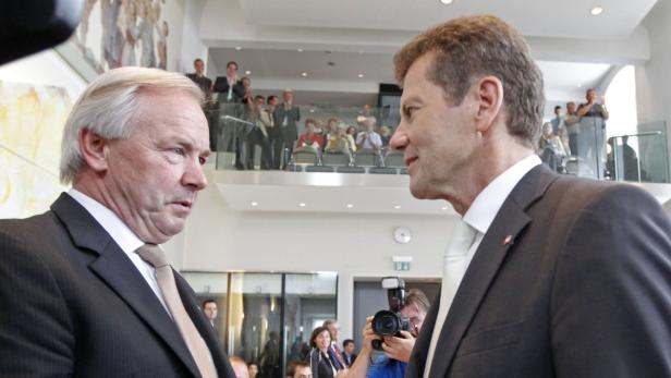 Zwei Männer in Anzügen unterhalten sich vor einer Zuschauertribüne.