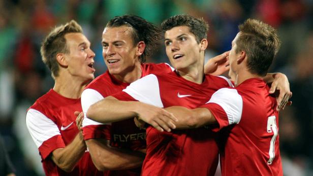 Vier Fußballspieler in roten Trikots umarmen sich und feiern.