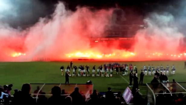 Ein Fußballstadion ist mit rotem Rauch und Feuerwerk gefüllt.