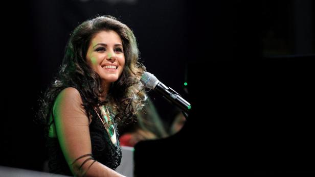 Eine lächelnde Sängerin steht am Mikrofon neben einem Klavier.