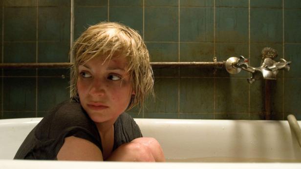 Eine verletzte Frau sitzt ängstlich in einer Badewanne.