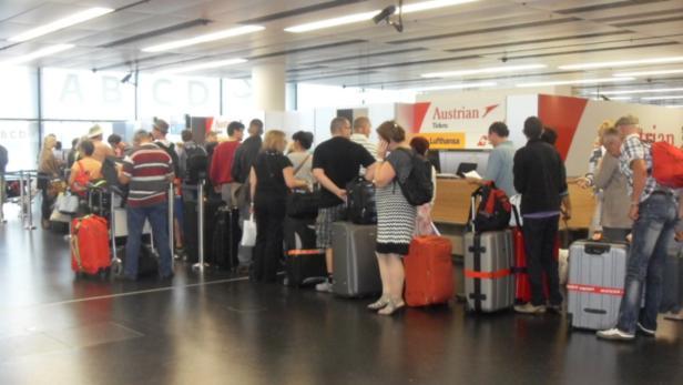 Reisende stehen mit Gepäck in einer Warteschlange am Check-in-Schalter von Austrian Airlines.