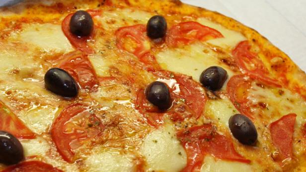 Eine Pizza mit Tomaten, Mozzarella und Oliven in einem Karton.