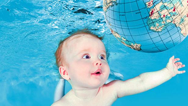 Ein Baby schwimmt unter Wasser und greift nach einem Globus.