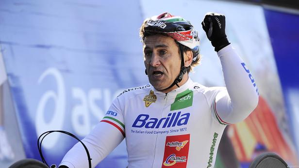Radfahrer mit Helm und Trikot der Marke Barilla jubelt mit erhobener Faust.