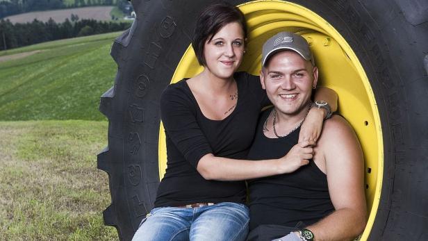 Ein junges Paar sitzt in einem Traktorreifen auf einem Feld.