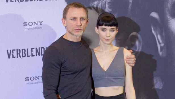 Daniel Craig und Rooney Mara posieren zusammen vor einer Filmkulisse.