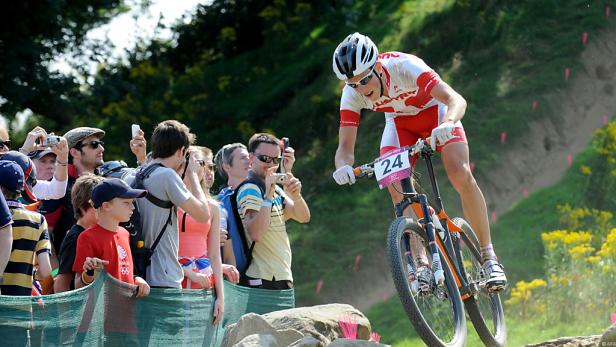 Ein Mountainbike-Fahrer mit der Nummer 24 fährt einen steinigen Parcours entlang, während Zuschauer zusehen.