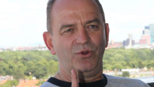 Ein Mann gestikuliert mit dem Finger vor einer Stadtlandschaft.