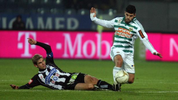 Ein Fußballspieler grätscht, während ein anderer den Ball kontrolliert.