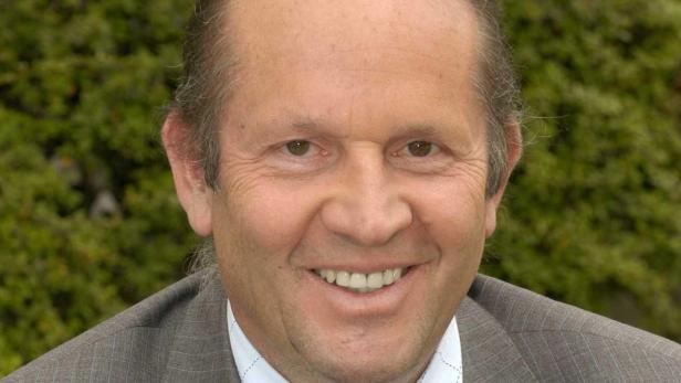 Ein lächelnder Mann in einem grauen Anzug vor einem grünen Hintergrund.