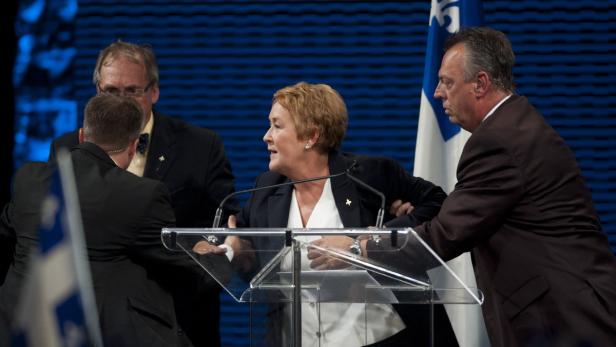 Zwei Männer führen Pauline Marois von der Bühne ab.