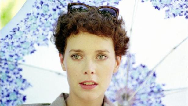 Eine Frau mit Sonnenbrille auf dem Kopf steht unter einem Sonnenschirm.