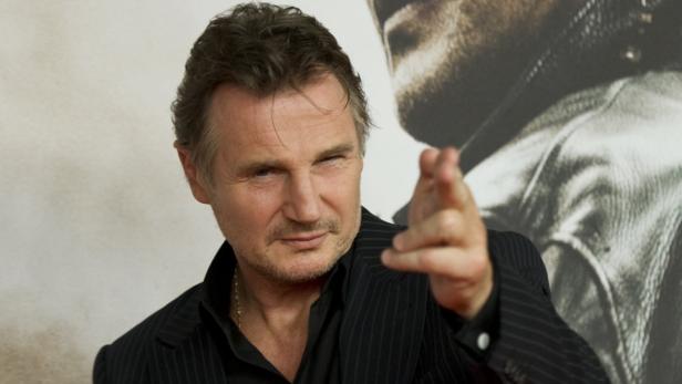 Liam Neeson posiert auf einem Foto und deutet mit dem Finger auf die Kamera.