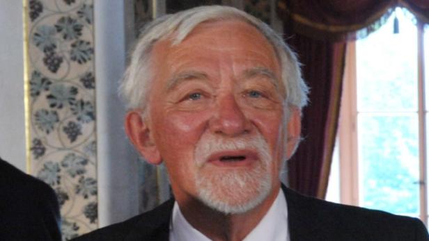 Ein älterer Mann mit weißem Haar und Bart in einem Anzug.