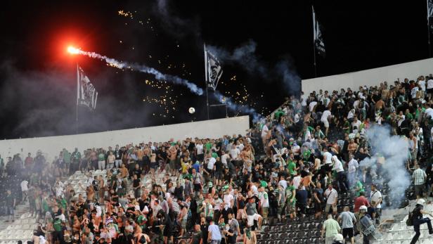 Auf der Tribüne eines Fußballstadions zünden Fans Rauchbomben und Bengalos.