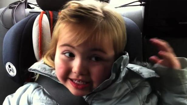 Ein kleines Mädchen sitzt angeschnallt in einem Autositz.